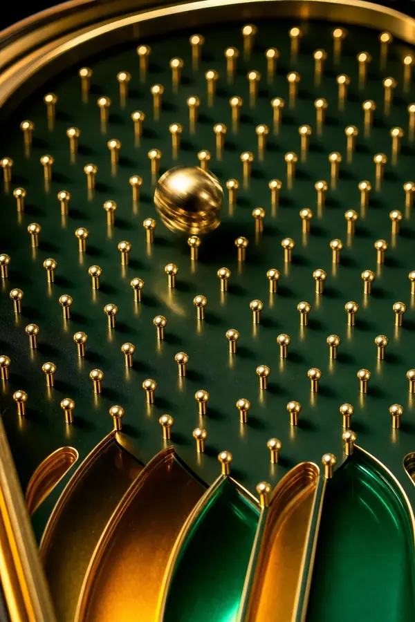 A golden ball bouncing through a field of brass pegs above amber and green channels